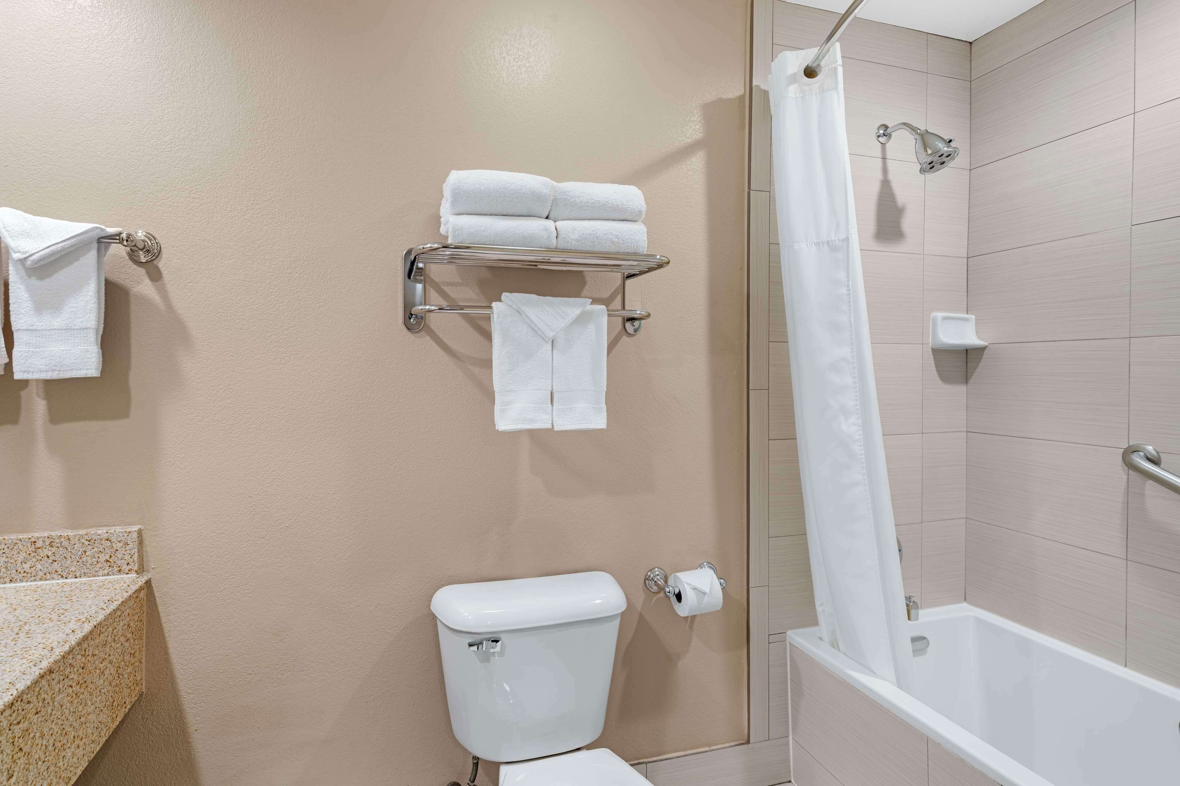 A bathroom with a toilet, a shower with a curtain, and a towel rack with folded towels.