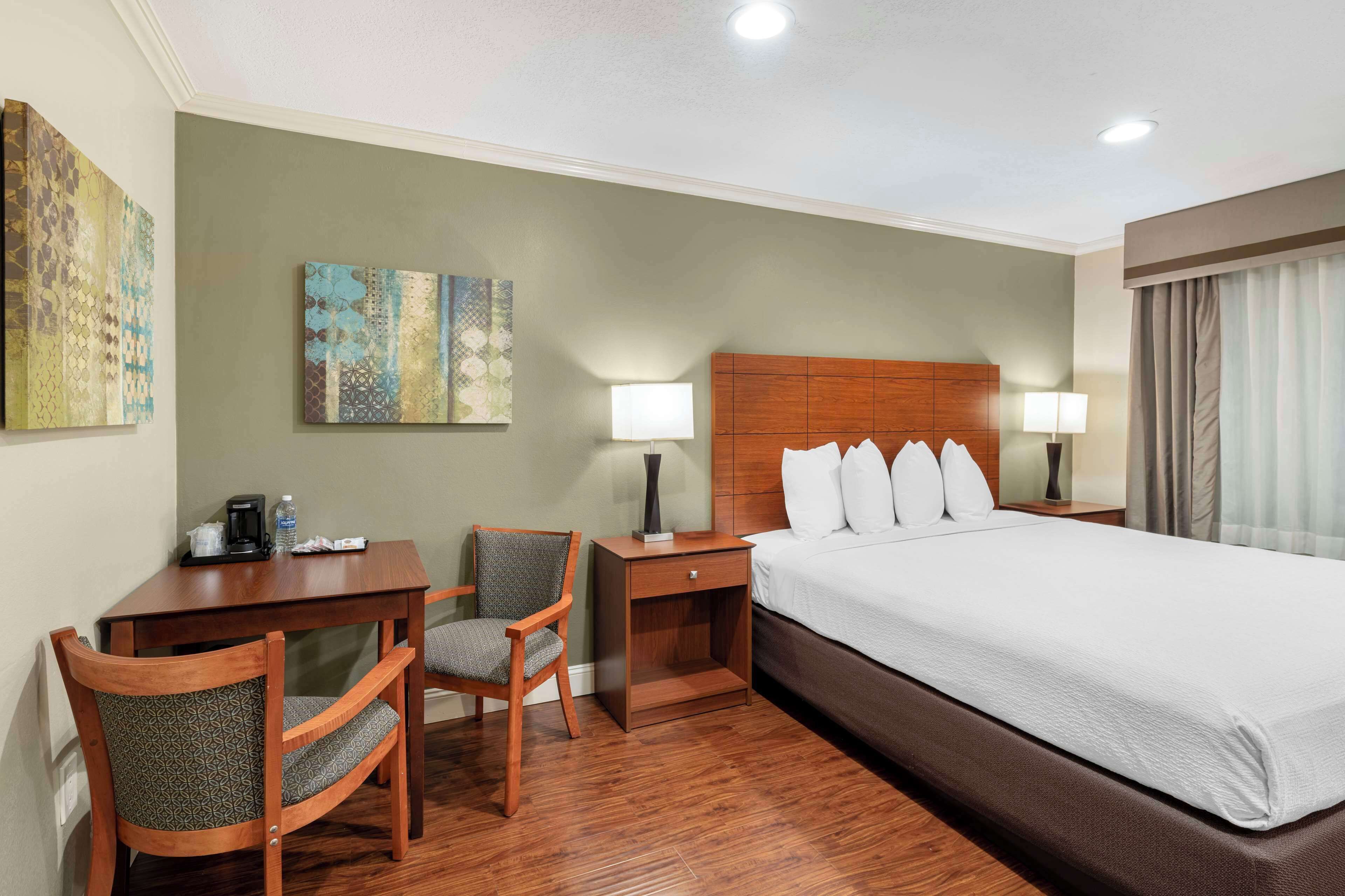 Habitación de hotel con cama, escritorio, silla, mesita de noche y dos lámparas de pared.