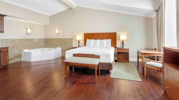A spacious bedroom with a large bed, a wooden bench, a bathtub, and a desk with chairs. - Best Western Oxnard Inn (Oxnard)