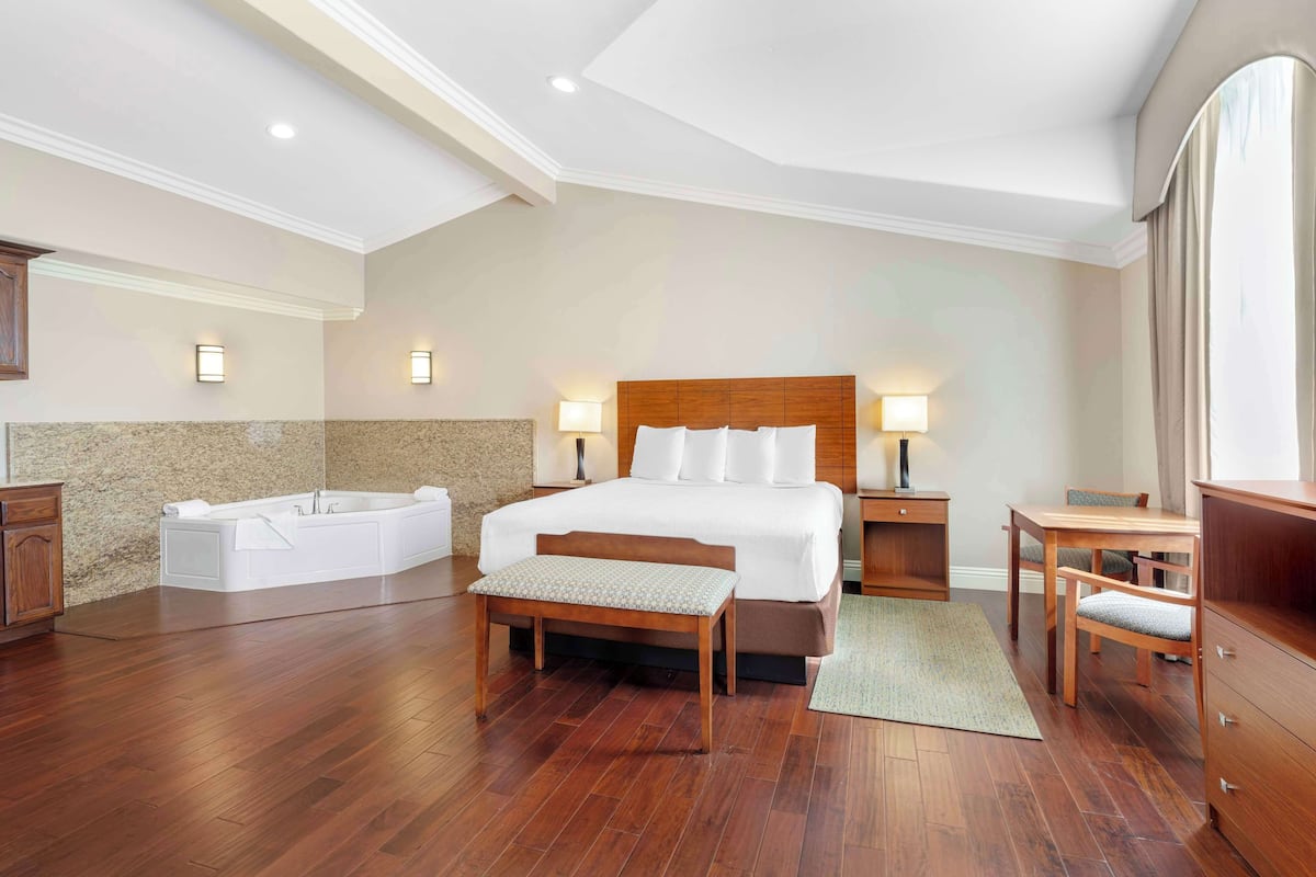 A spacious bedroom with a large bed, a wooden bench, a bathtub, and a desk with chairs.