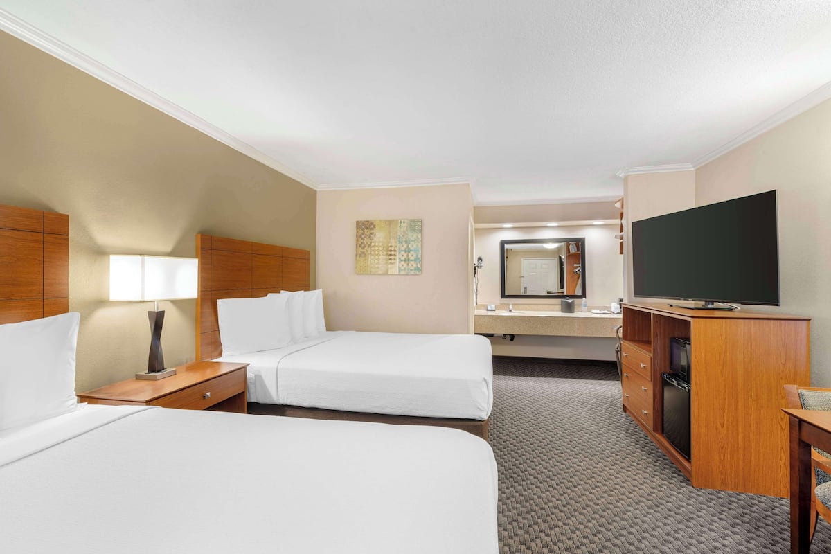 A hotel room with two beds, a TV, a desk, and a mirror.