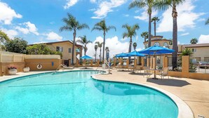 A swimming pool with lounge chairs and umbrellas, surrounded by palm trees and buildings. - Best Western Oxnard Inn (Oxnard)