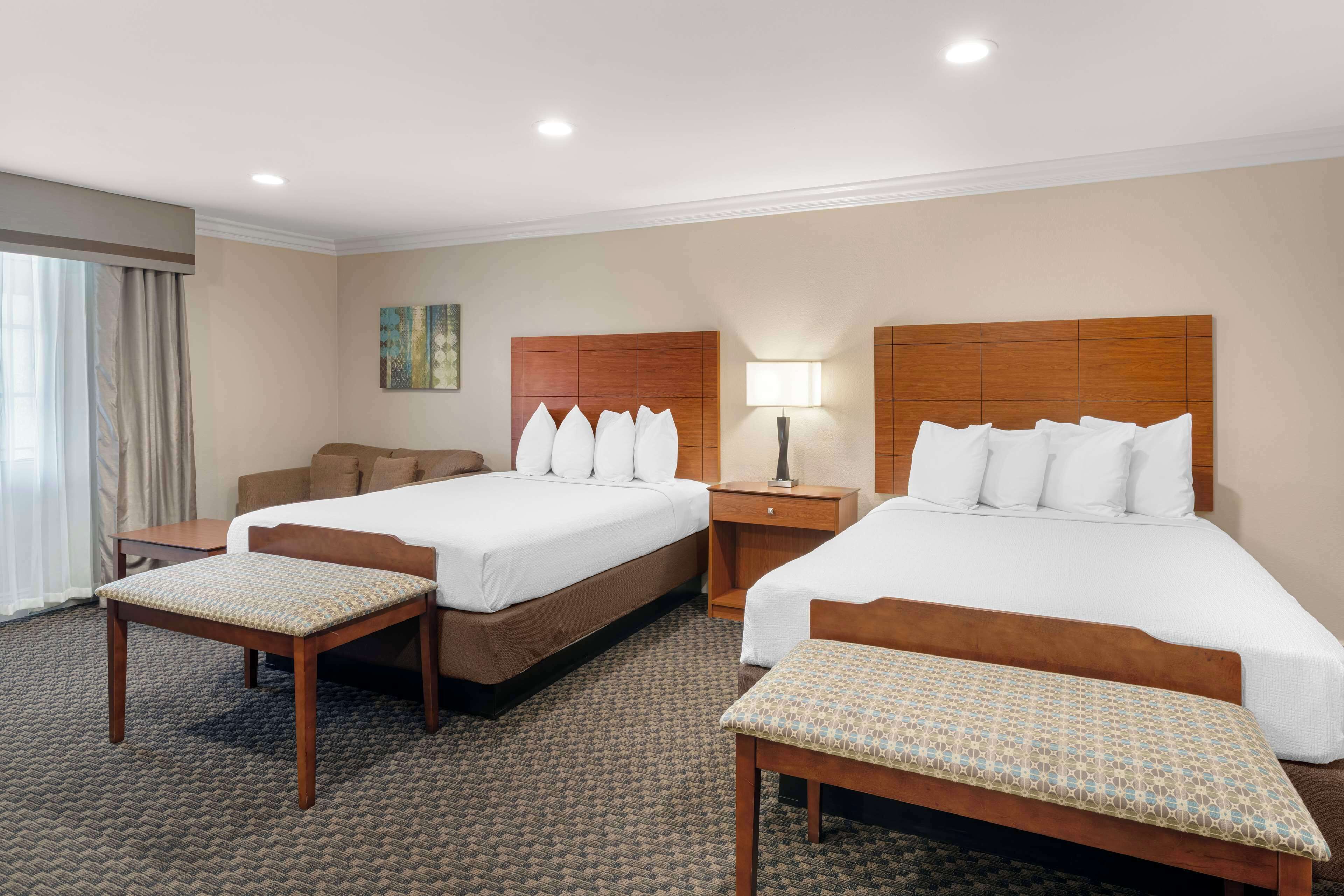 Habitación de hotel con dos camas, un escritorio, una silla y un banco.
