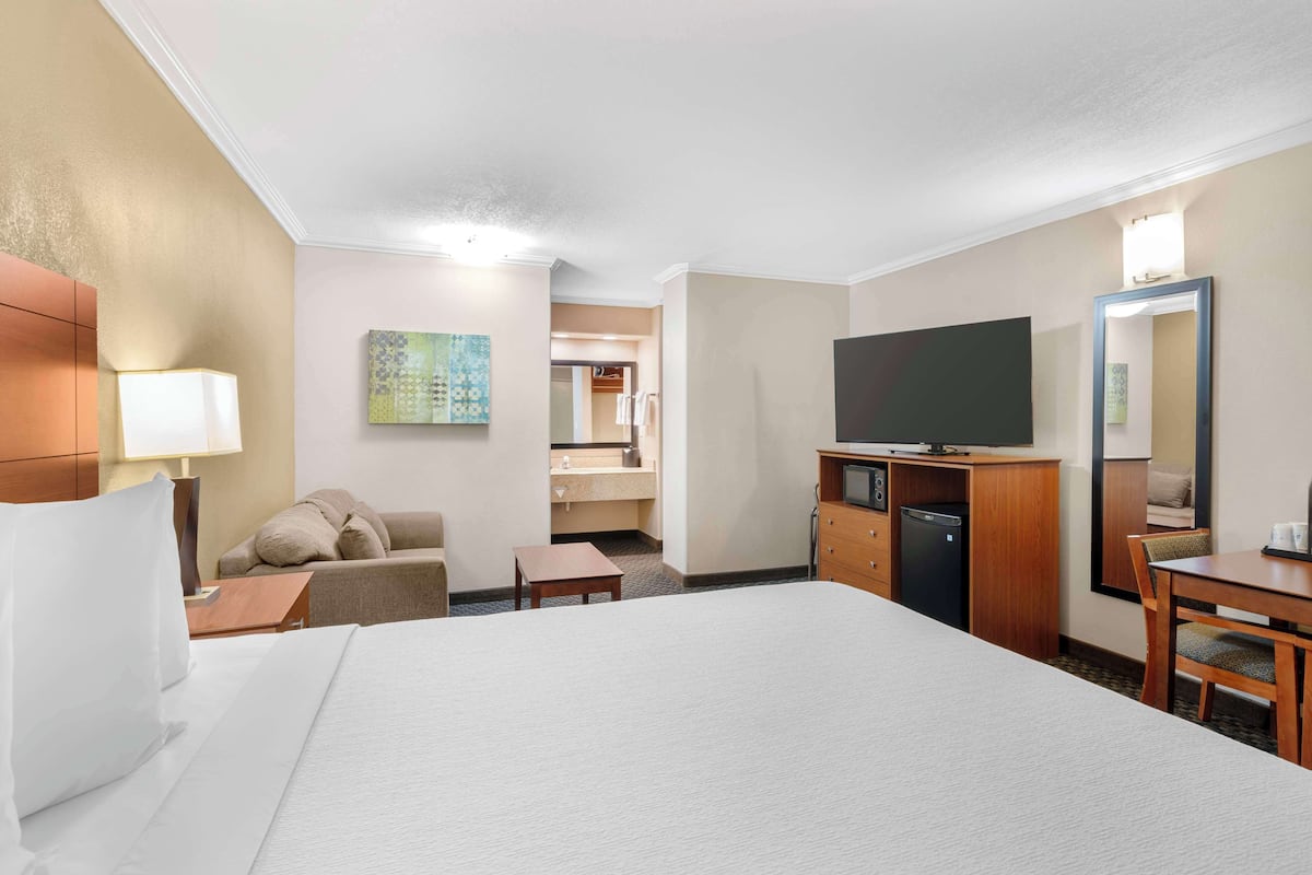 A hotel room with a bed, a desk, a television, a dresser, and a small table.