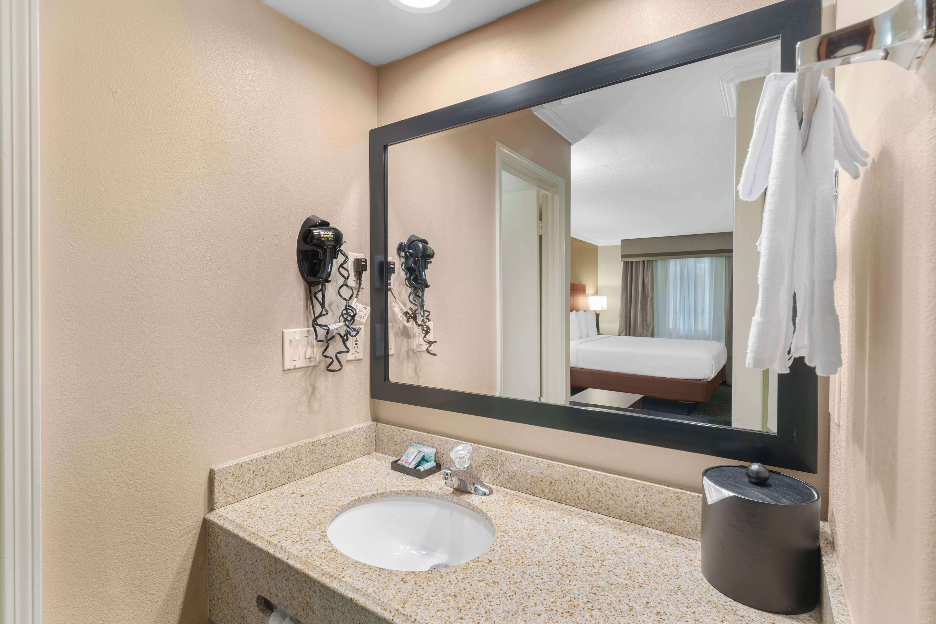 Um banheiro de hotel com um espelho grande, uma pia e um secador de cabelo na parede.