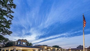 A hotel with a prominent American flag, a covered entrance, and a well-lit facade. - Days Inn & Suites by Wyndham Williamsburg Colonial (Williamsburg)