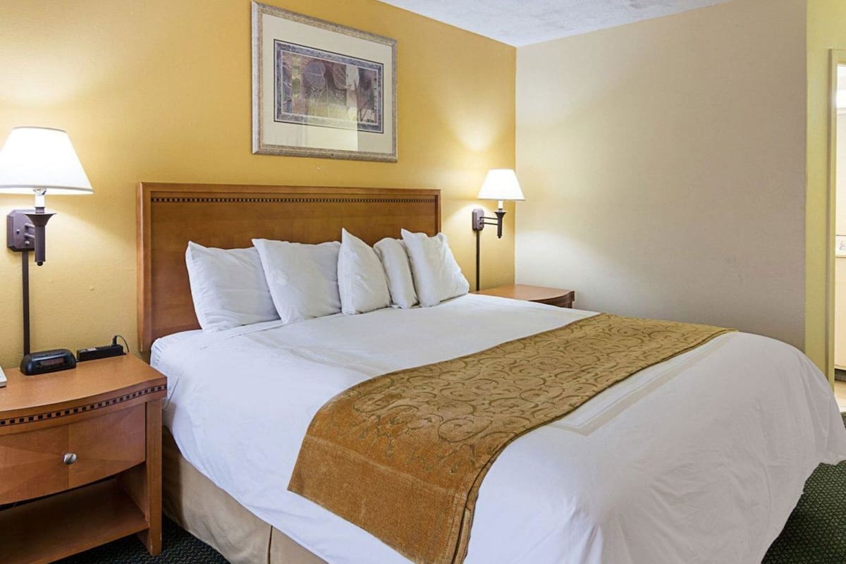 A hotel room with a large bed, two bedside lamps, a nightstand, a framed picture on the wall, and a door to the right.