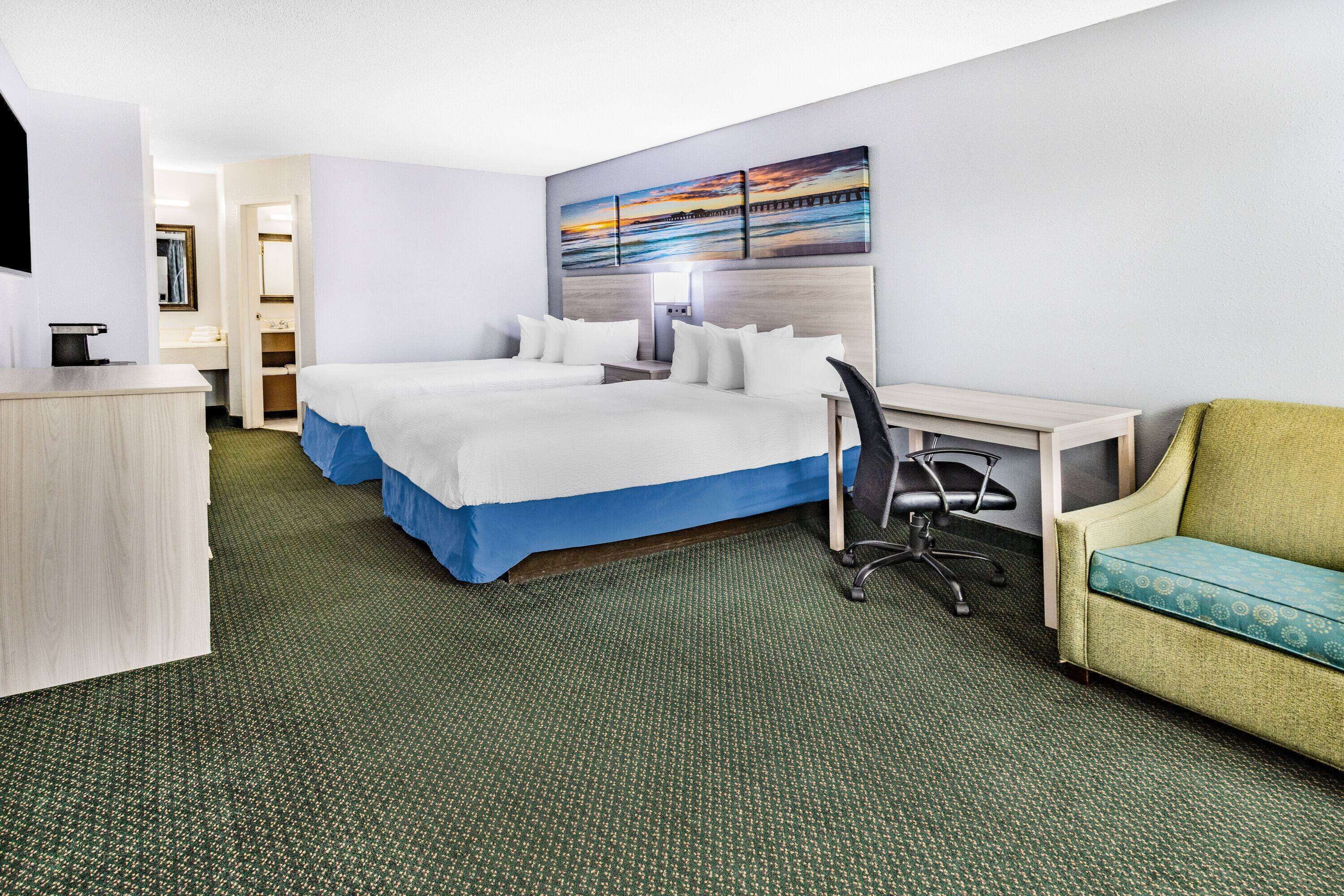 A hotel room with two beds, a desk, a chair, and a sofa.