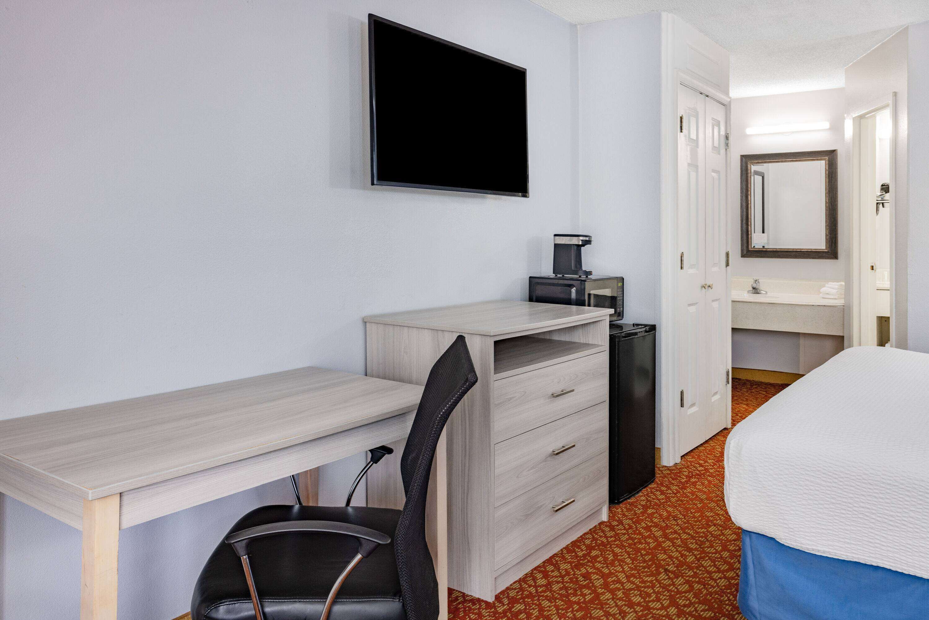 A hotel room with a desk, chair, TV, and a bed.