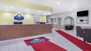 A reception area with a tiled wall, a reception desk, a red carpet, and a TV mounted on the wall. - Days Inn & Suites by Wyndham Williamsburg Colonial (Williamsburg)