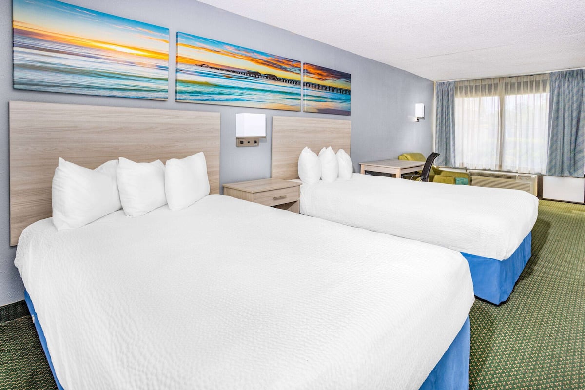 A hotel room with two beds, a desk, a chair, and a window with curtains.