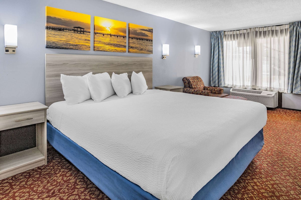 A hotel room with a large bed, a nightstand, a chair, and a window with curtains.