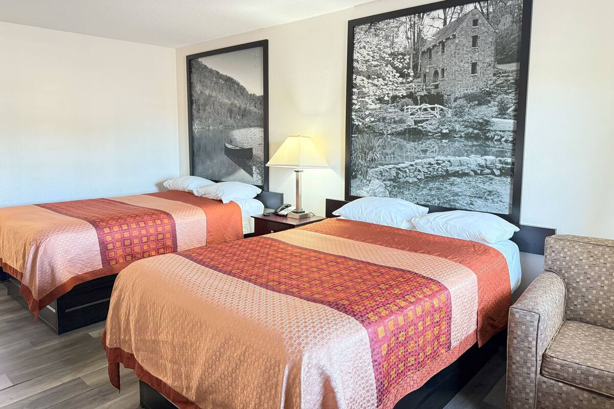 Ein Hotelzimmer mit zwei Betten, einem Nachttisch mit Lampe, einem Sessel und zwei großen Schwarz-Weiß-Fotos an der Wand.