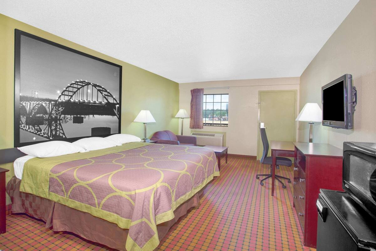 Ein Hotelzimmer mit Bett, Schreibtisch, Stuhl, Fernseher und einem großen, gerahmten Bild einer Brücke.