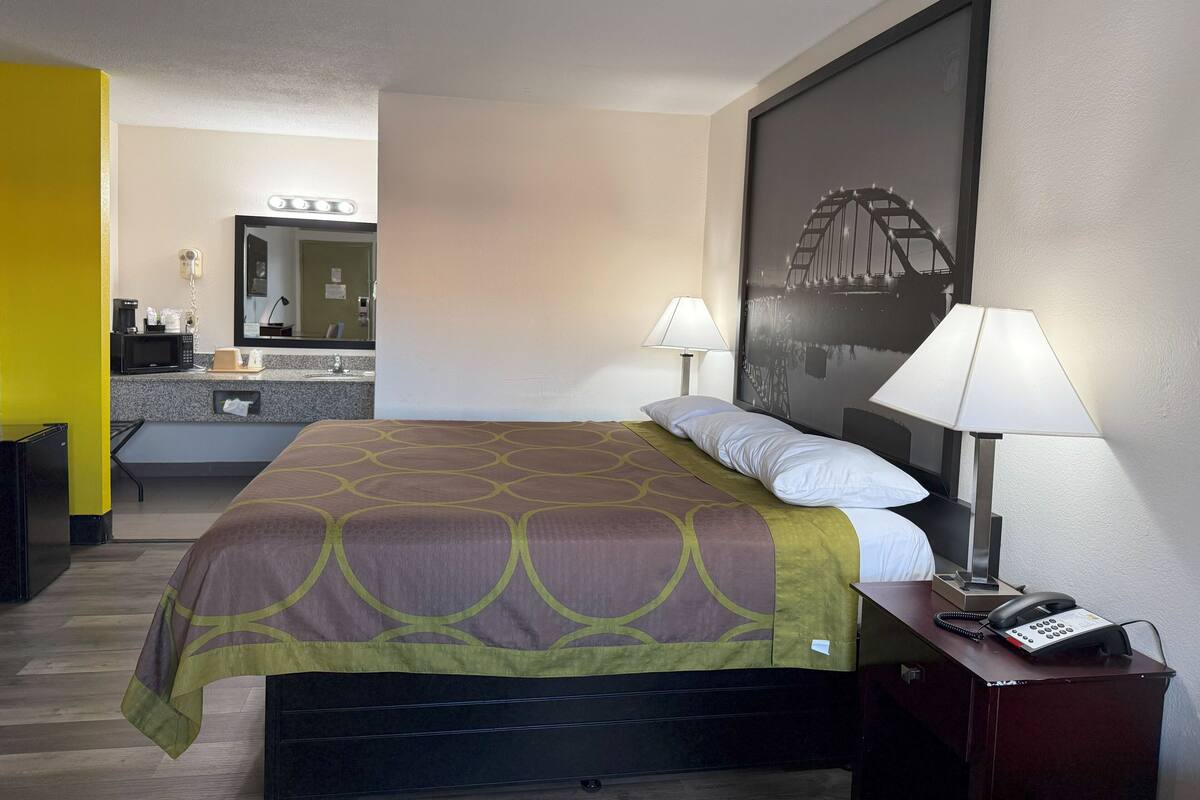 Ein Hotelzimmer mit einem Bett, Nachttischlampen, einem Telefon und einem großen, gerahmten Bild an der Wand.