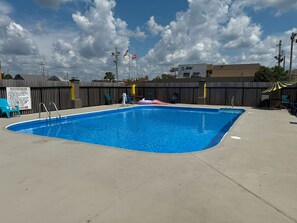 A swimming pool with a fenced area, lounge chairs, and a sign with swimming pool rules.