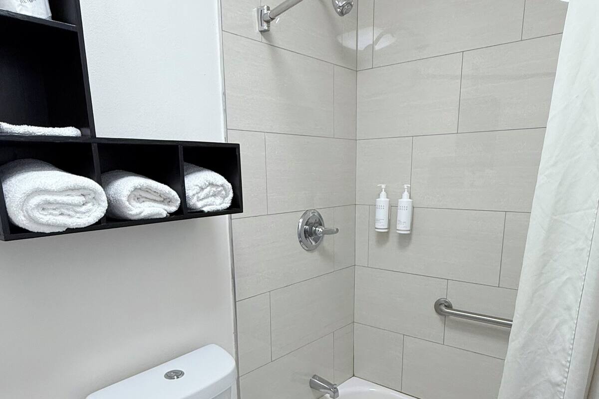 Ein modernes Badezimmer mit Toilette, Badewanne und Dusche. Handtücher und Pflegeprodukte liegen auf Regalen.