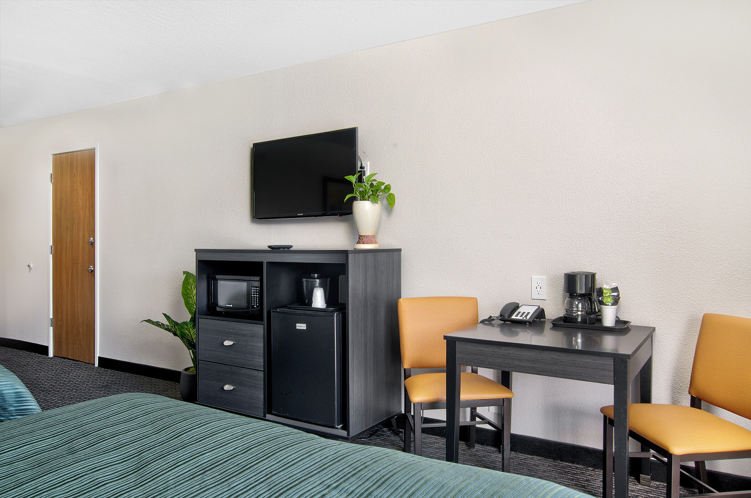 Habitación de hotel con cama, escritorio, dos sillas, televisor, cafetera y refrigerador.