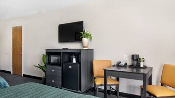 Habitación de hotel con cama, escritorio, dos sillas, televisor, cafetera y refrigerador.