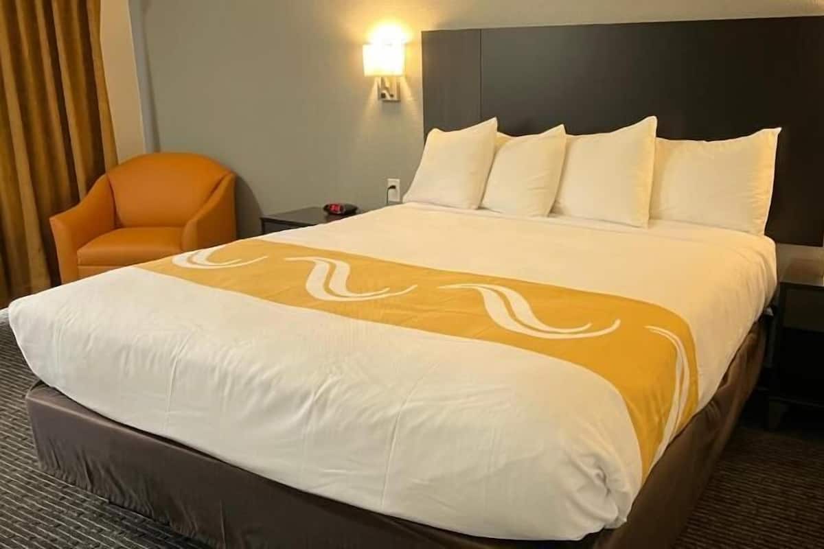 Een hotelkamer met een groot bed, een nachtkastje, een stoel en twee wandlampen.