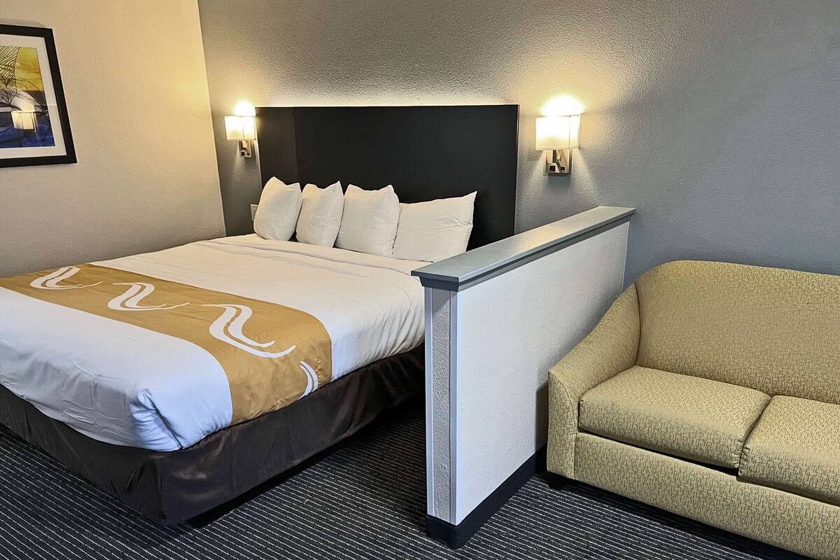 Een hotelkamer met een bed, hoofdeinde, twee wandlampen, een bank en een vloerkleed.