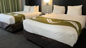 Una habitació d'hotel amb dos llits, cadascun amb roba de llit blanca i detalls verdosos, un panell de capçal fosc i una làmpada subjecta a la paret.