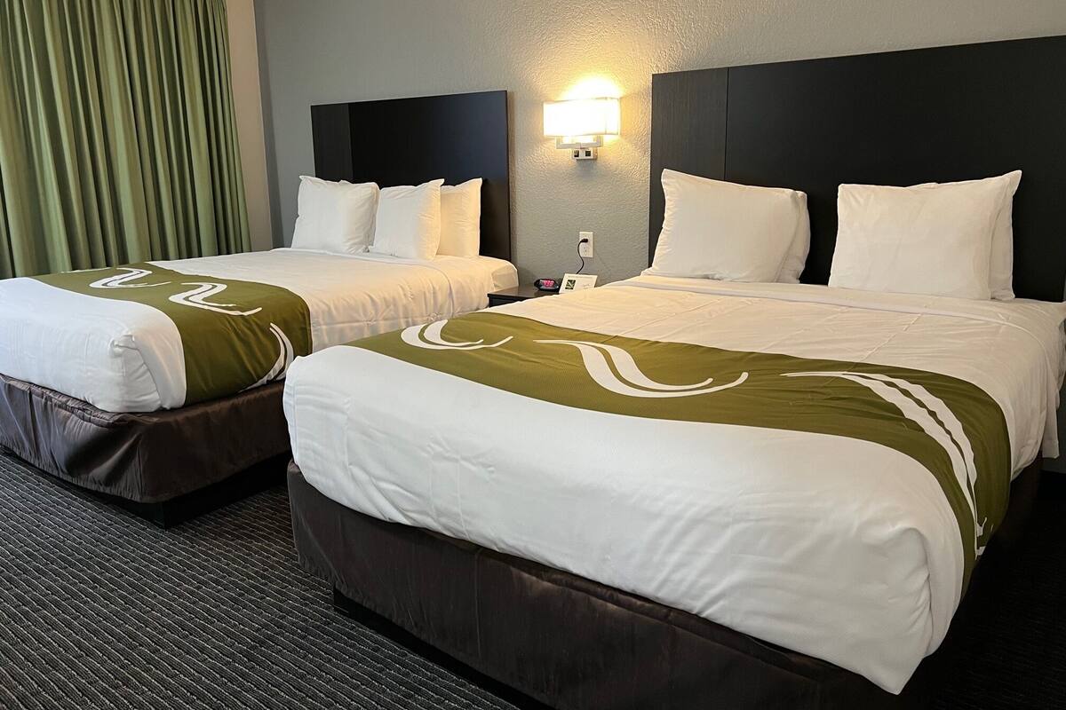 Een hotelkamer met twee bedden, elk voorzien van witte beddengoed en groene accenten, een donker hoofdeinde en een wandlamp.
