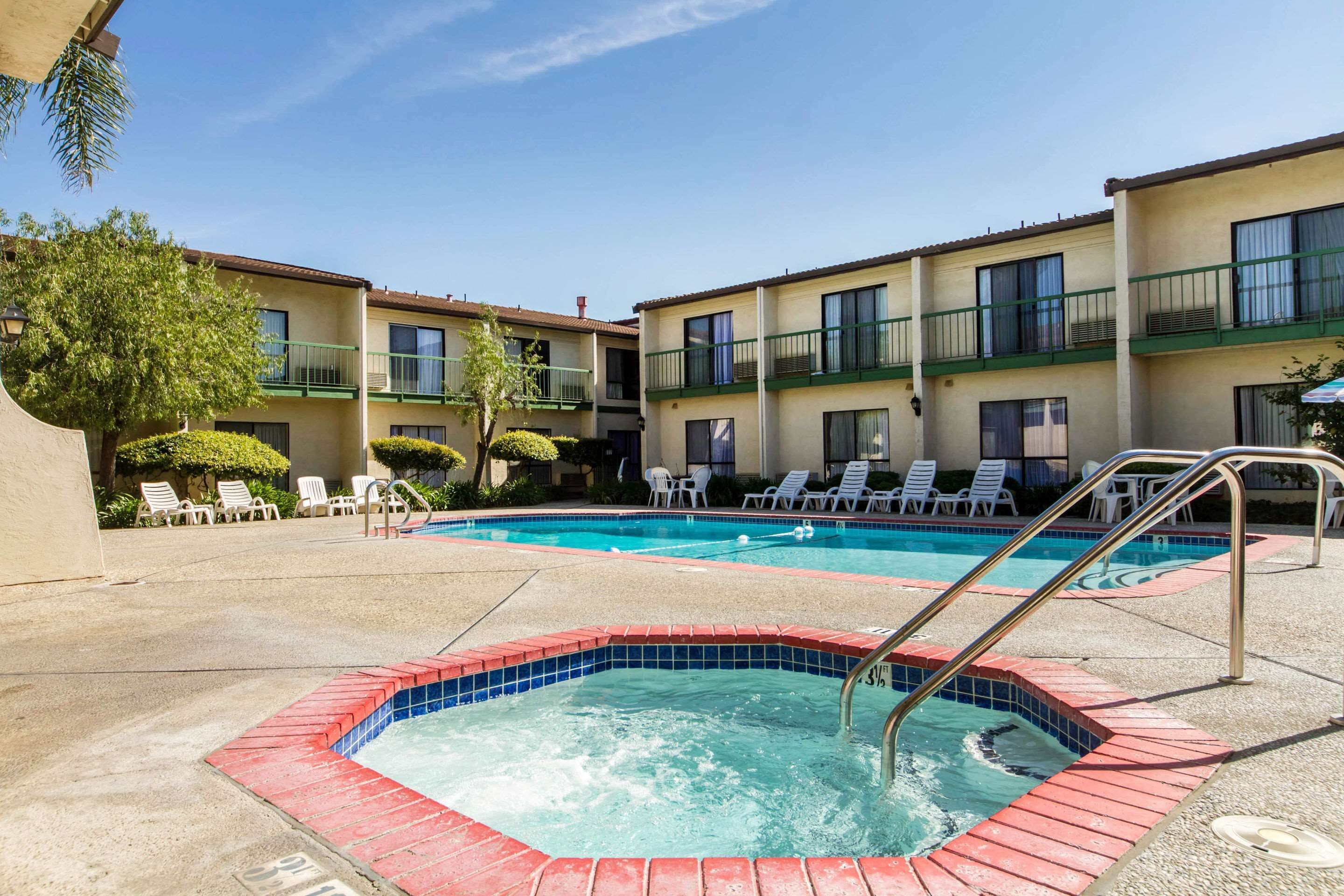 Une piscine avec un jacuzzi, des chaises longues et un bâtiment doté de balcons.