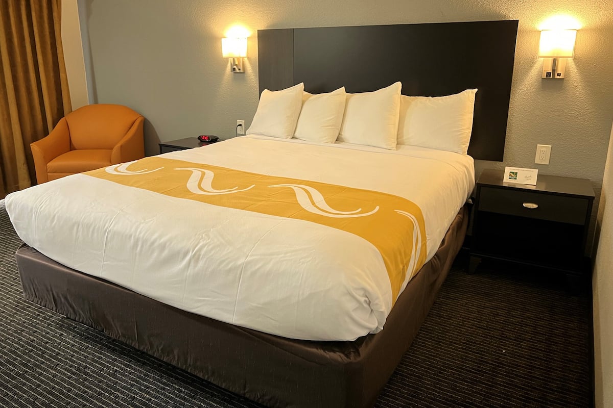 Een hotelkamer met een groot bed, twee nachtkastjes, een stoel en twee wandlampen.