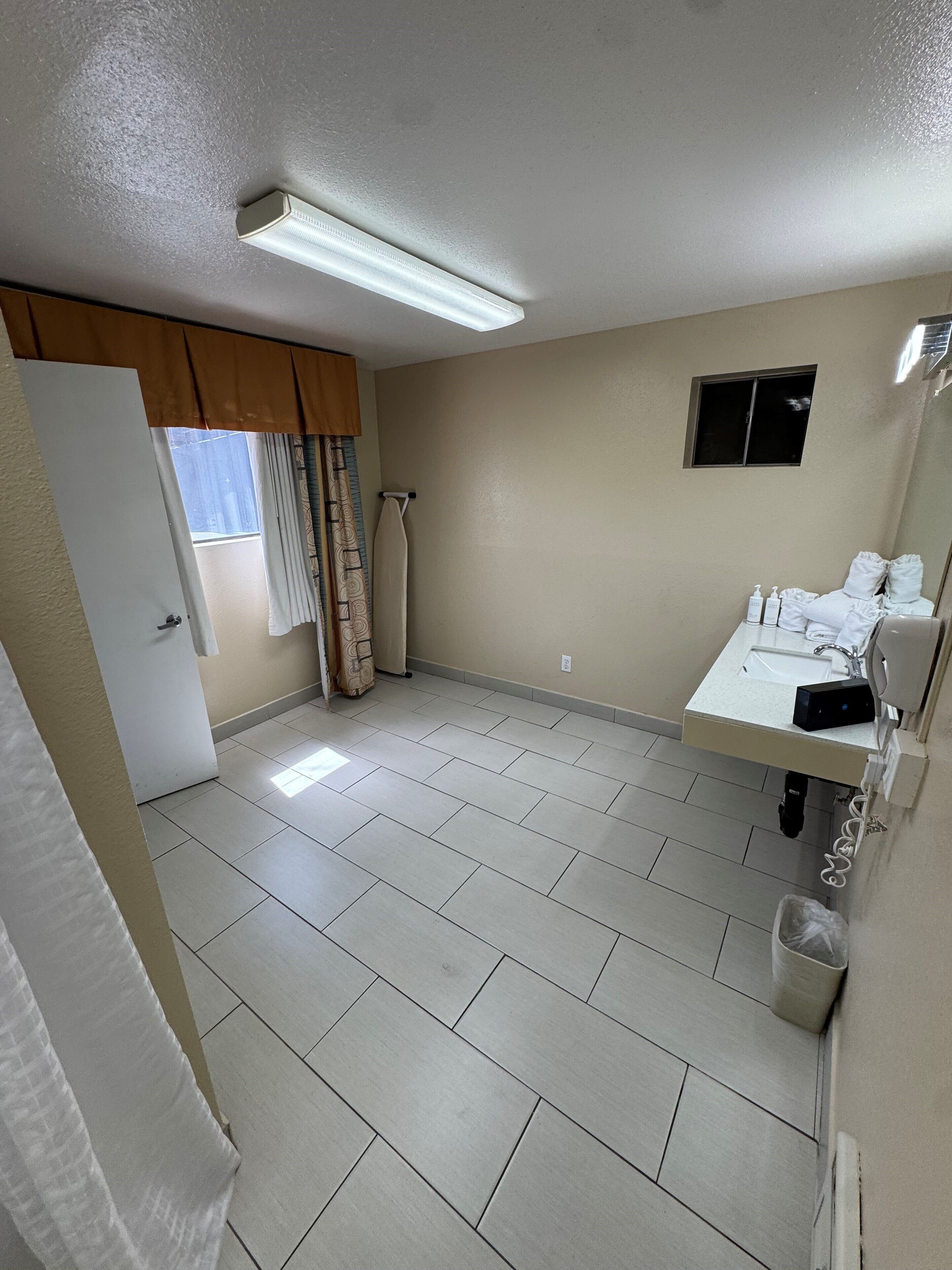 A bathroom with a white sink, mirror, and towel rack. There is a window with curtains and a towel hanging on the wall.