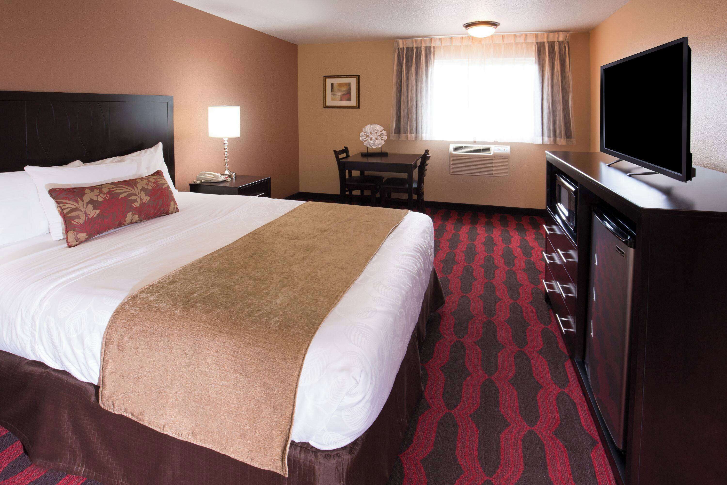 Quarto de hotel com uma cama grande, uma escrivaninha com cadeira, televisão e minibar.