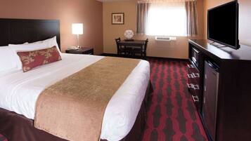 Quarto de hotel com uma cama grande, uma escrivaninha com cadeira, televisão e minibar.