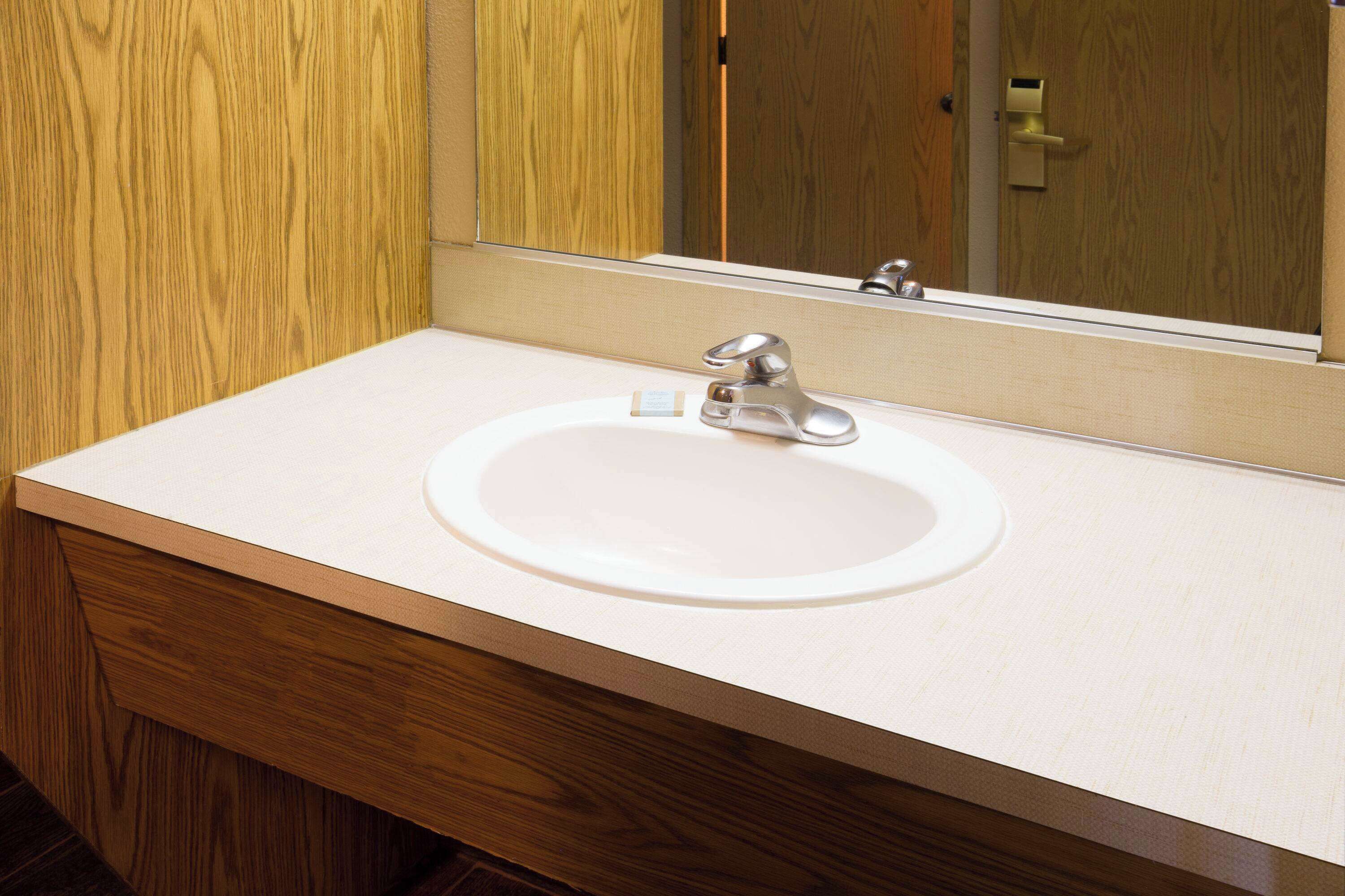 Un baño con tocador de madera, un lavabo blanco y un espejo encima.