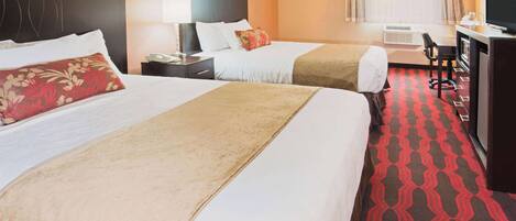 A hotel room with two beds, a desk, a TV, and an air conditioning unit.
