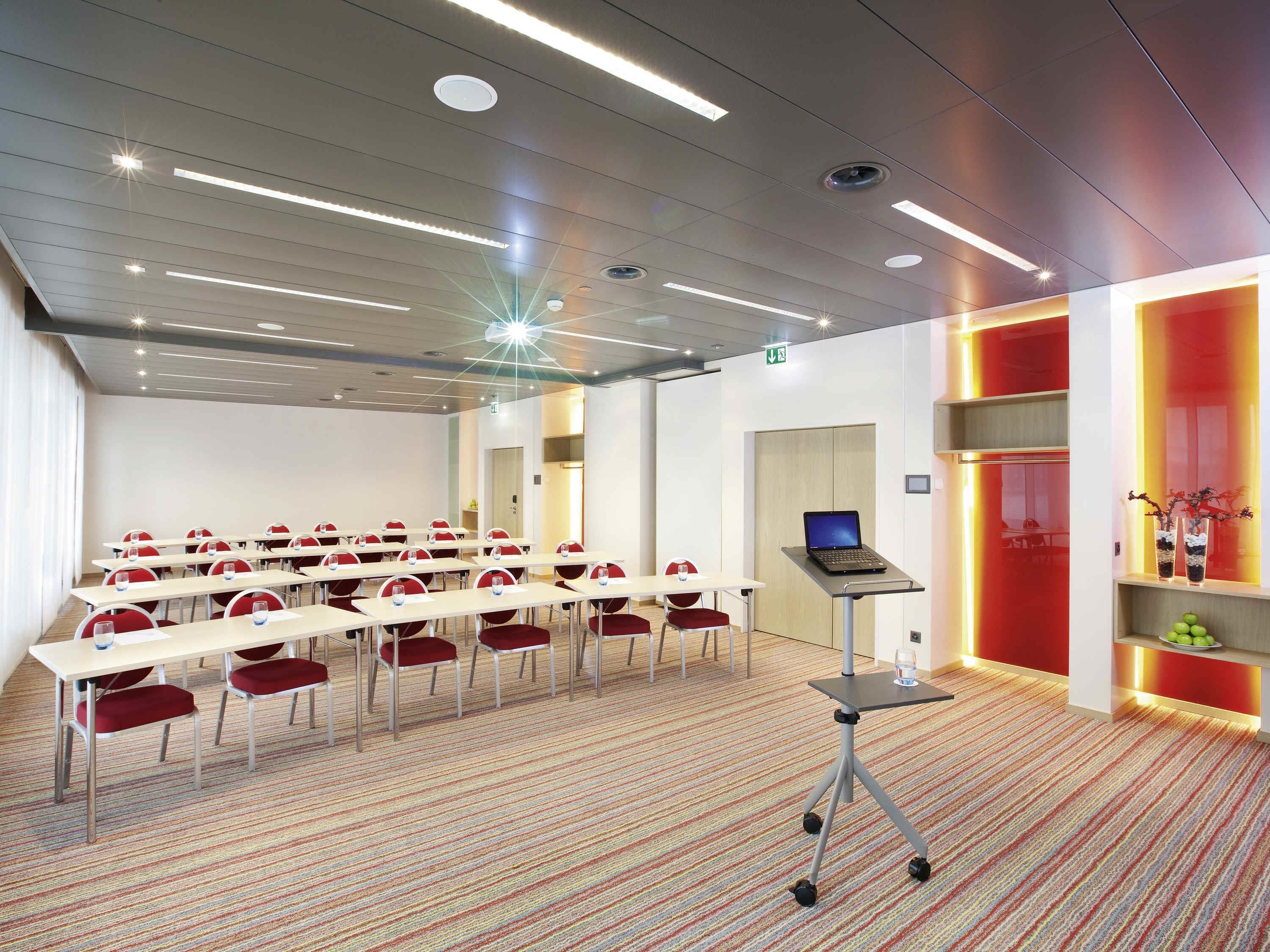 A conference room with tables, chairs, a laptop on a cart, and a carpeted floor.