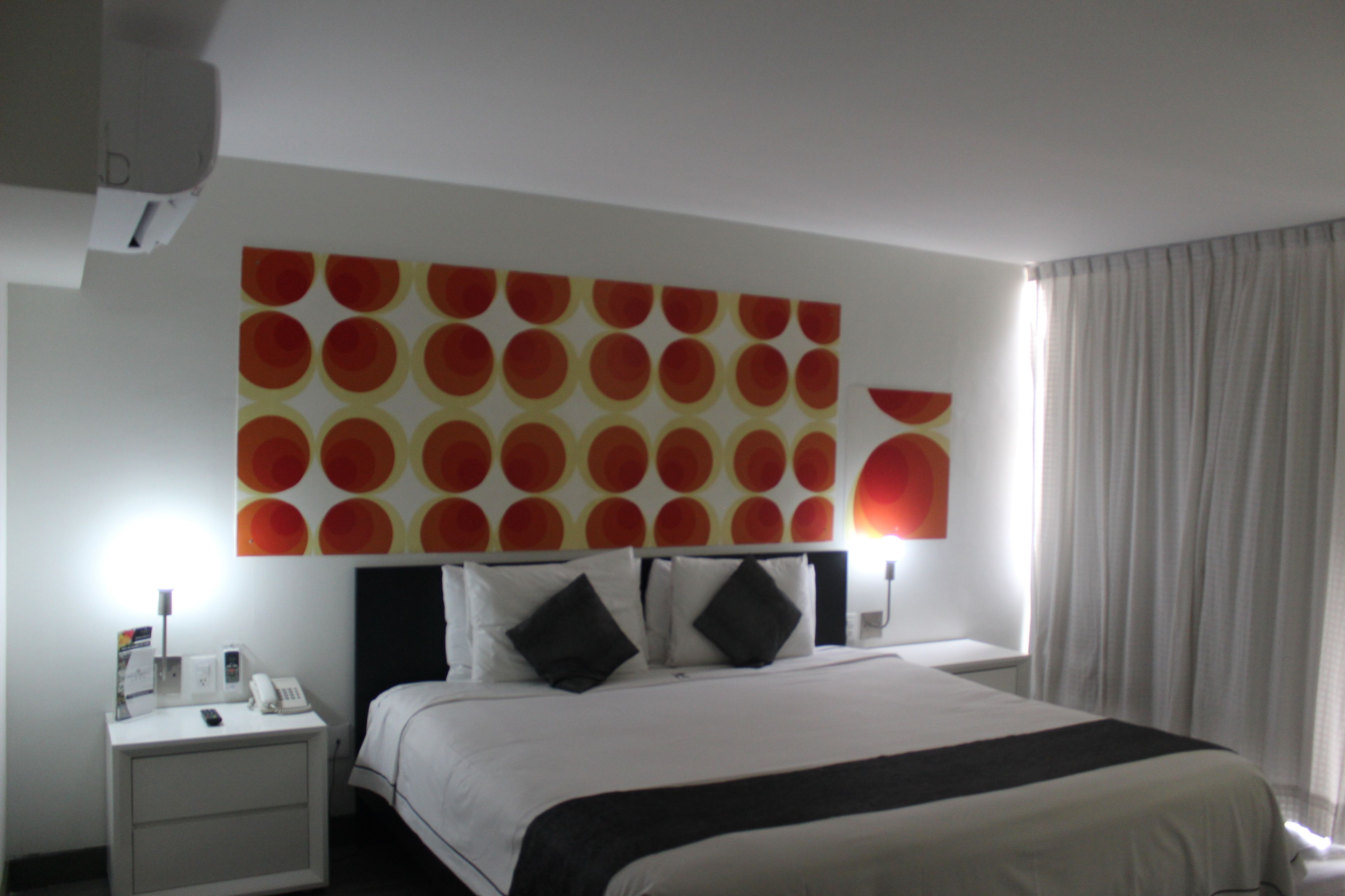 A hotel room with a large bed, a nightstand with a phone, and a wall with a circular pattern.