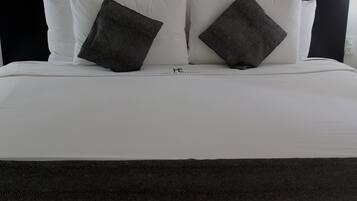 A neatly made bed with white linens and two dark gray pillows.