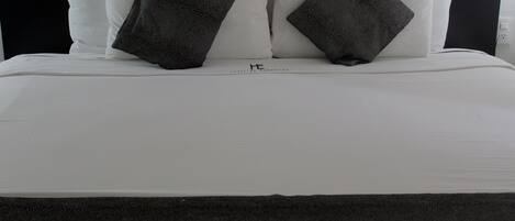 A neatly made bed with white linens and two dark gray pillows.