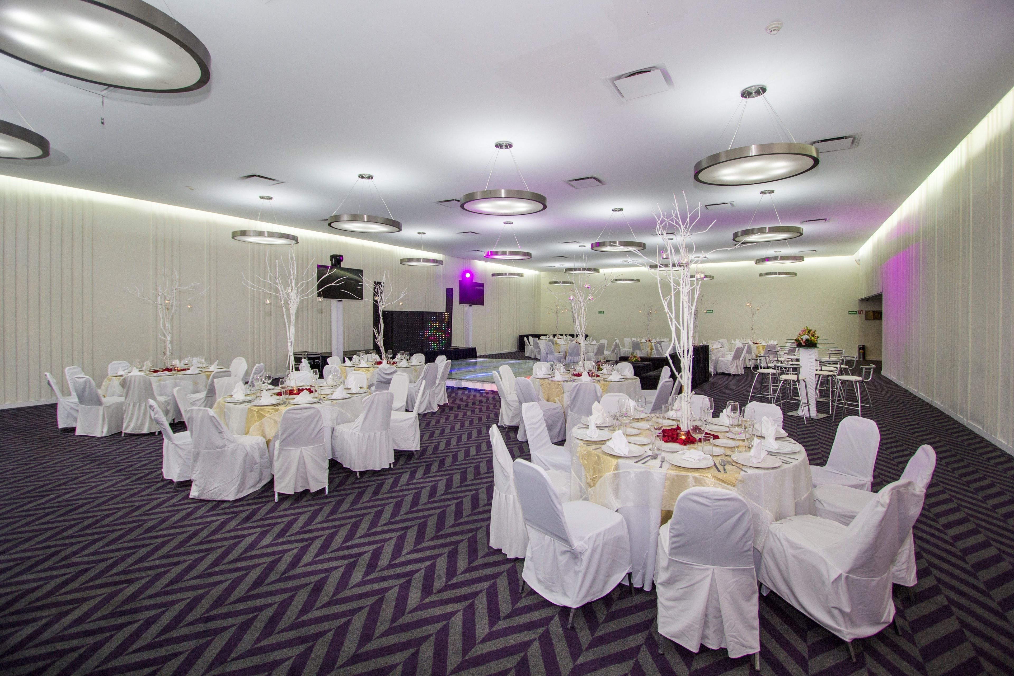 A banquet hall with round tables set for events, white chairs, and modern lighting fixtures.