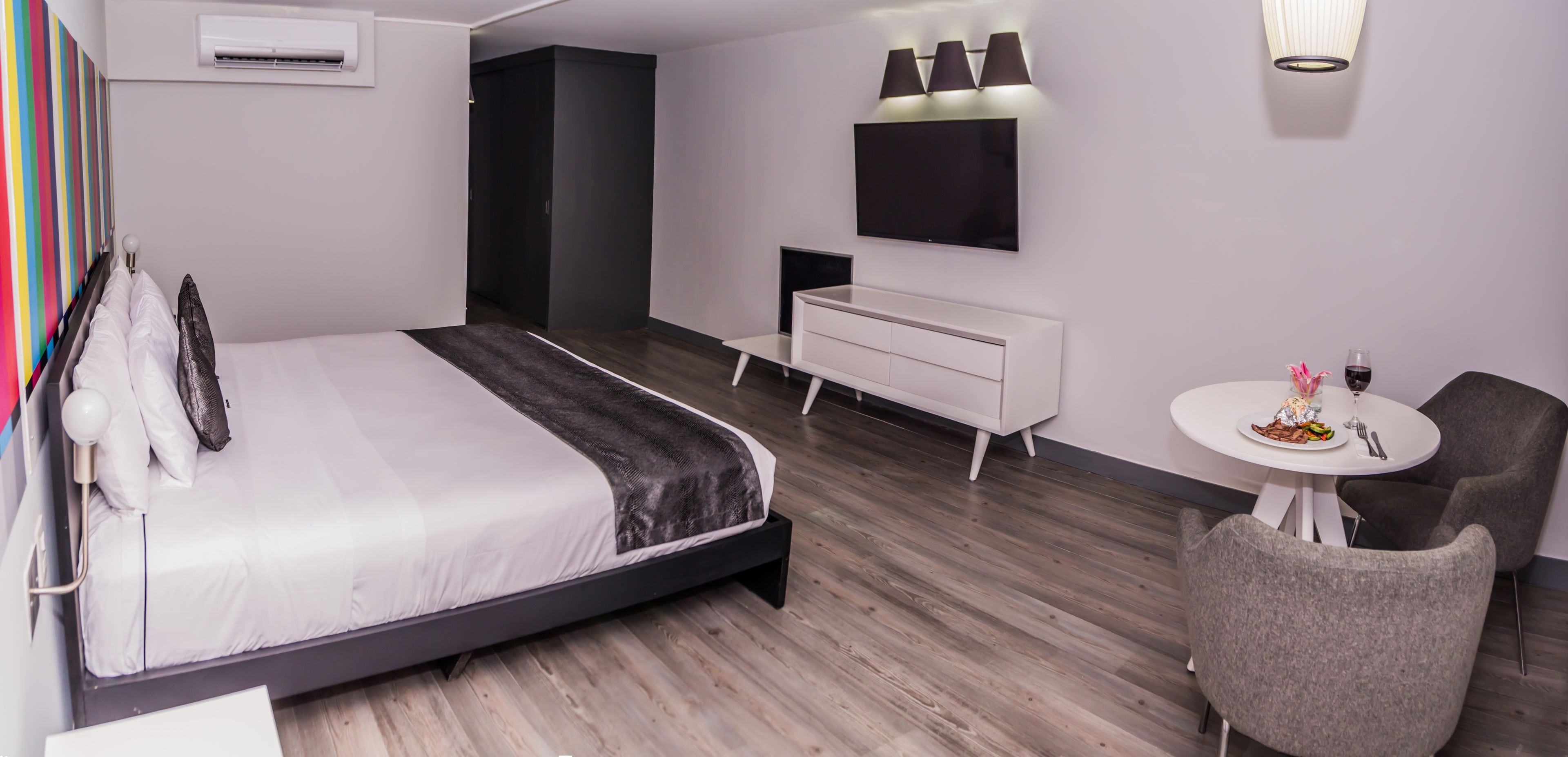 Moderni hotellihuone, jossa on suuri sänky, pieni työpöytä, televisio sekä ruokailutila, jossa on pöytä ja tuolit.