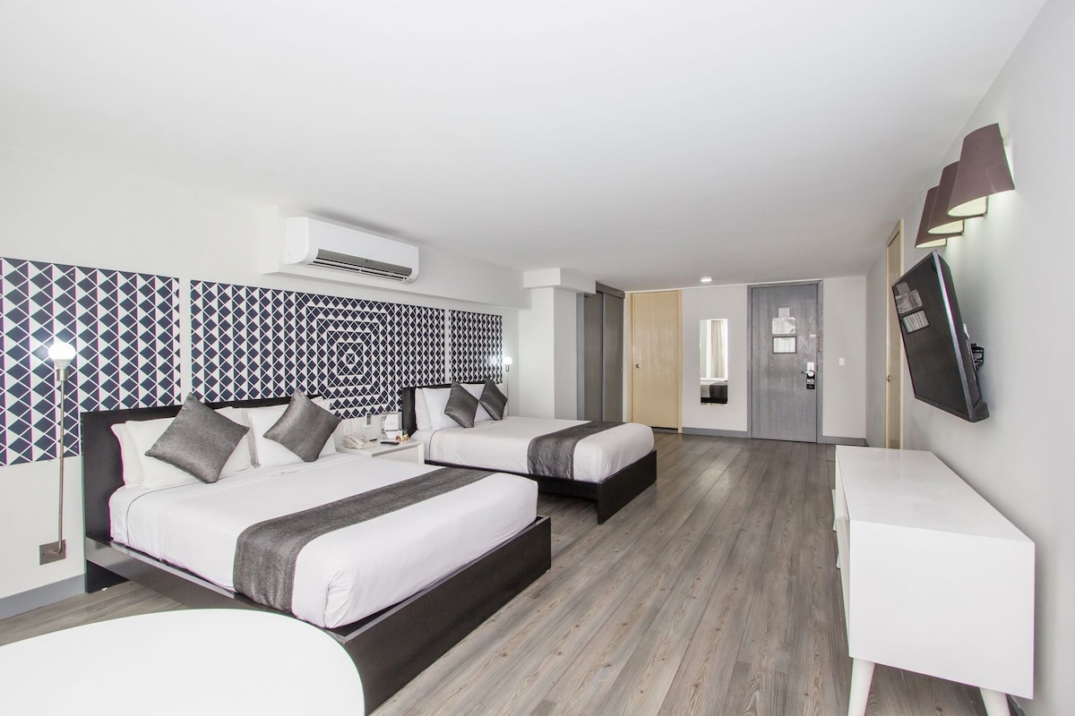 Habitación de hotel con dos camas, un escritorio, un televisor y un aire acondicionado.