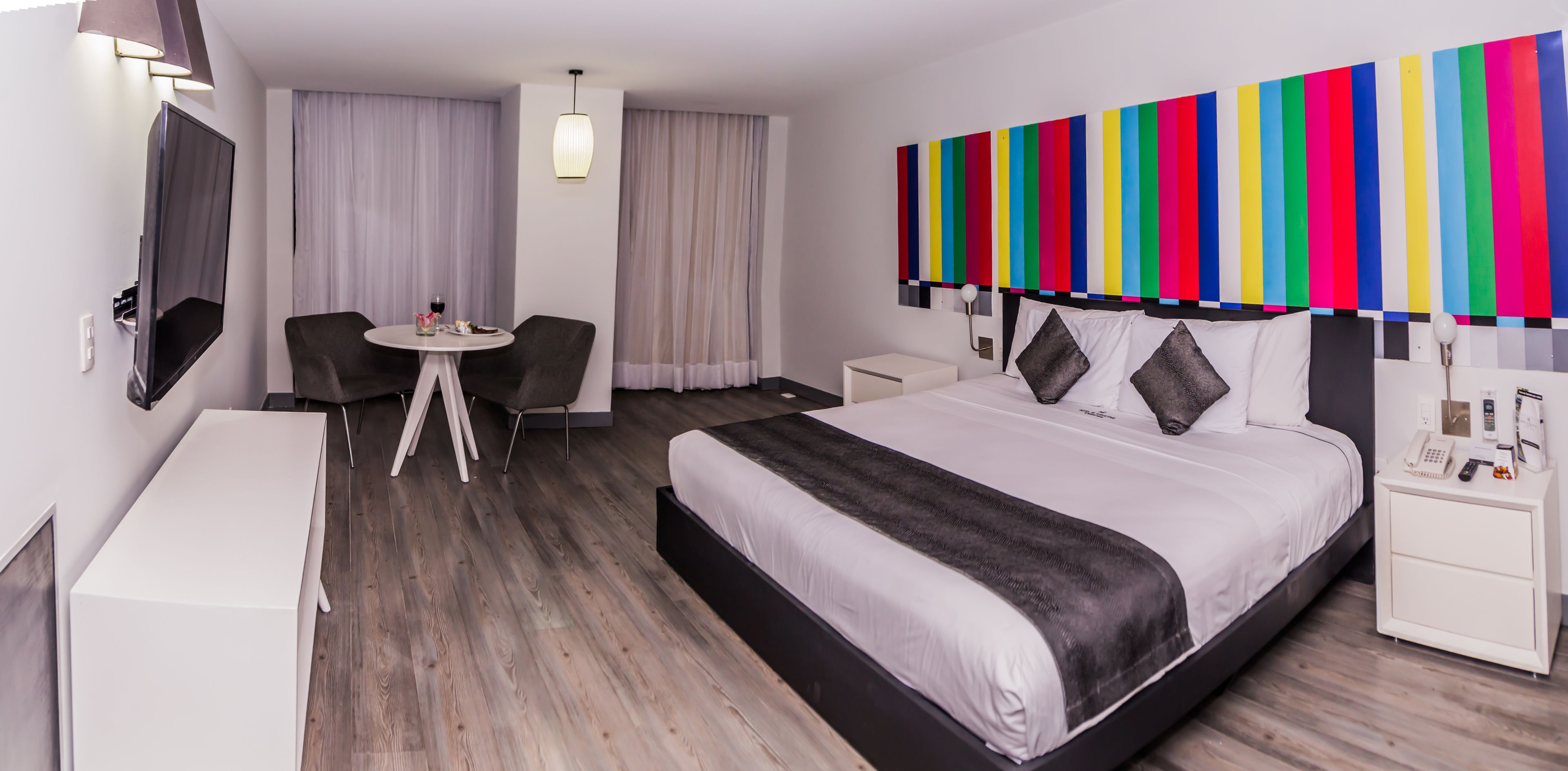 A hotel room with a large bed, a desk with a chair, a TV, and a colorful wall decoration.