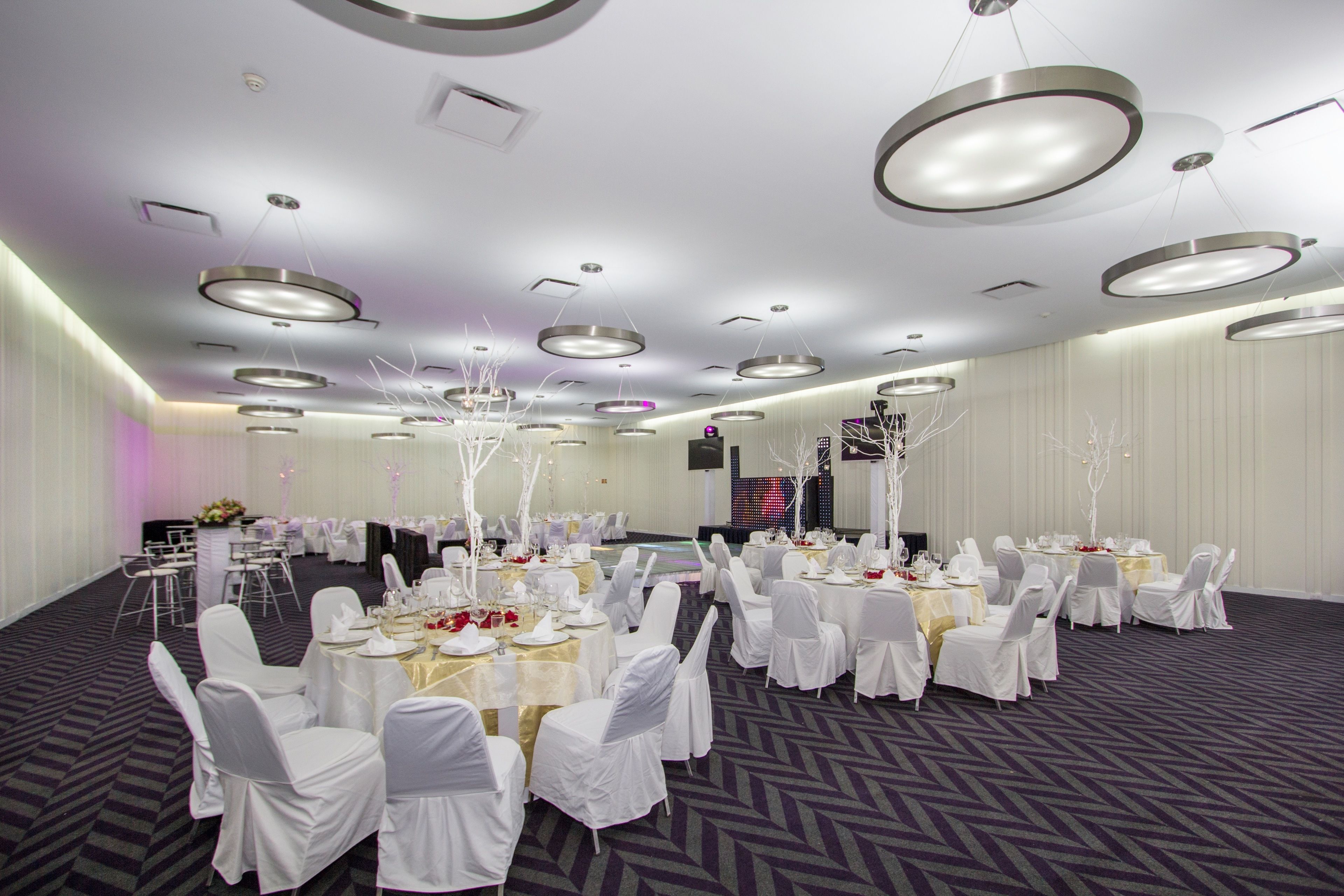 A banquet hall with round tables, white chairs, and a modern ceiling design.