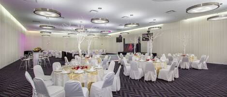 A banquet hall with round tables, white chairs, and a modern ceiling design.