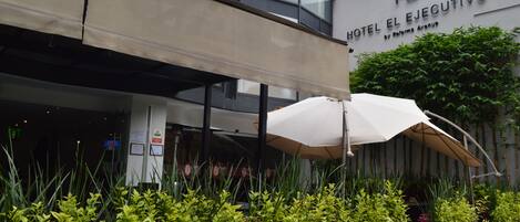 A hotel entrance with a covered outdoor seating area, potted plants, and a sign for Hotel El Ejecutivo.