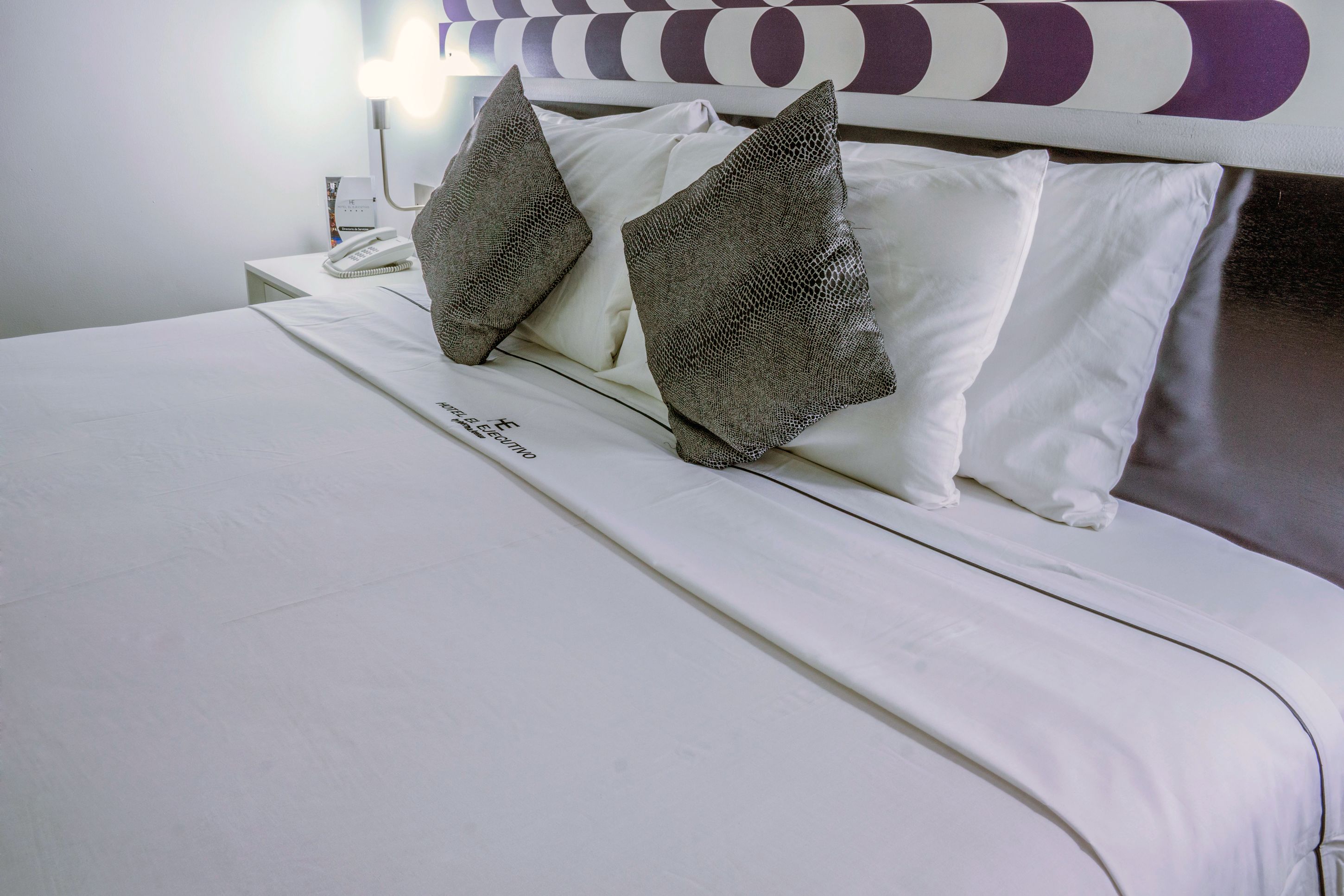 Una cama bien tendida con ropa blanca y dos almohadas con textura.