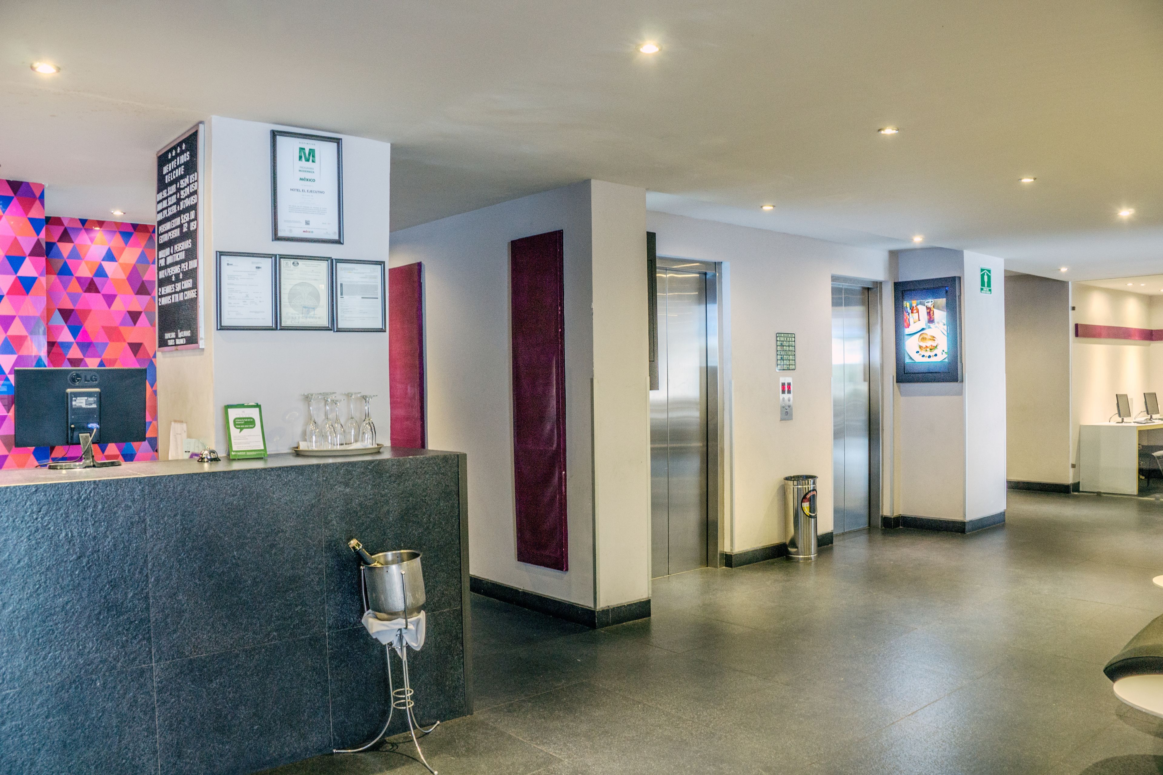 A hotel reception area with a modern design, including a reception desk, framed certificates, and a colorful geometric wall.
