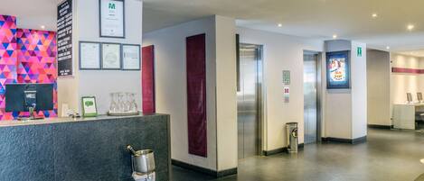 A hotel reception area with a modern design, including a reception desk, framed certificates, and a colorful geometric wall.