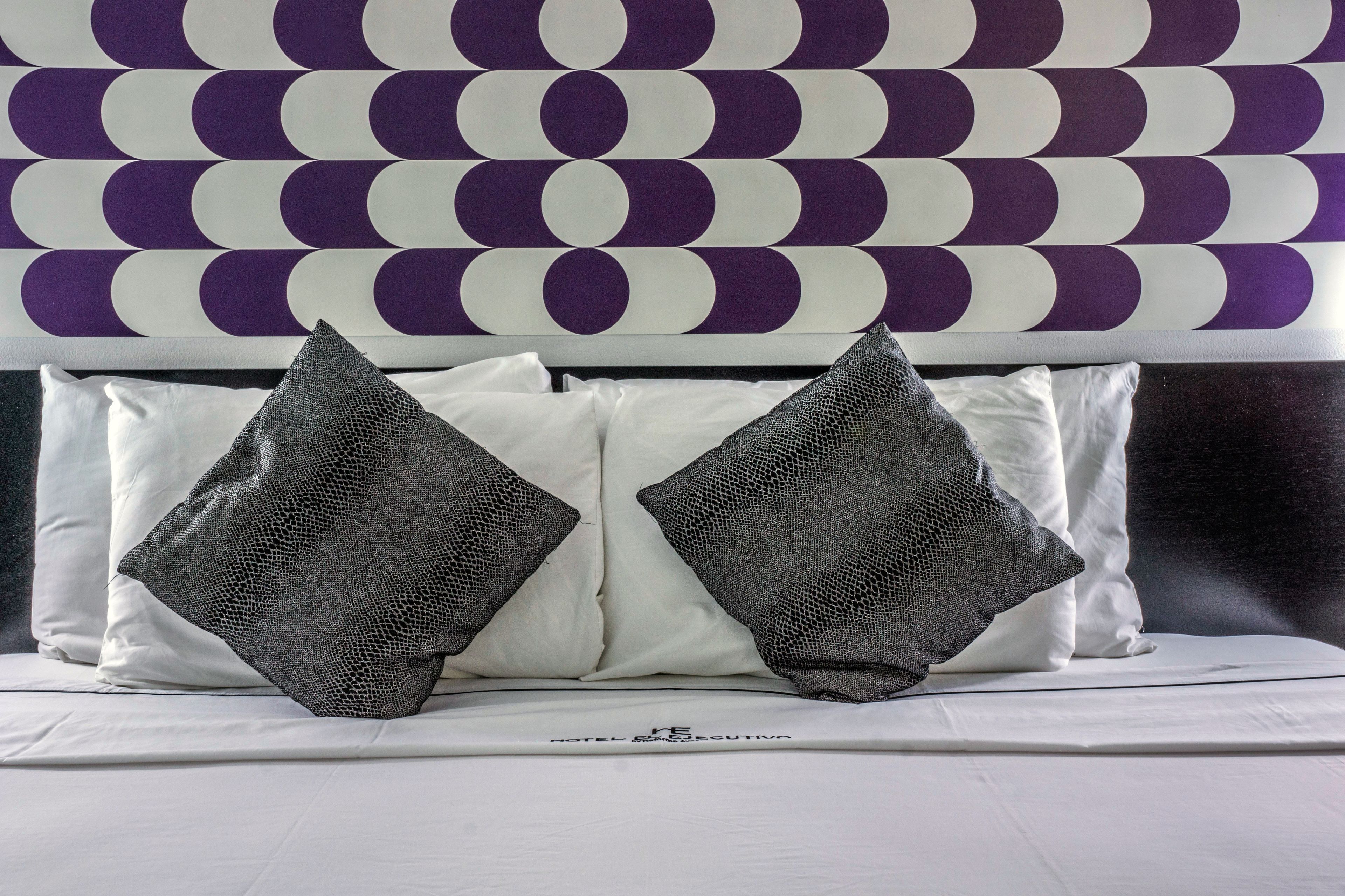 A bed with white bedding and two grey pillows, a headboard with a circular pattern, and a logo on the headboard.