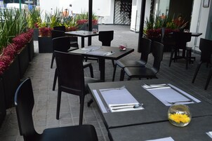 Un espace extérieur aménagé pour les repas, avec des tables et des chaises, entouré de plantes et de fleurs en pot.